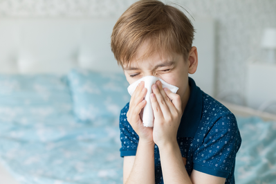 young boy blowing nose into a tissue