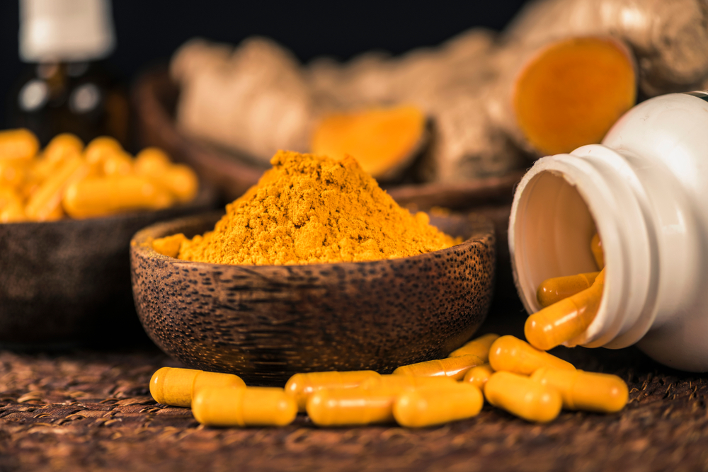 curcumin powder and capsules in front of turmeric root