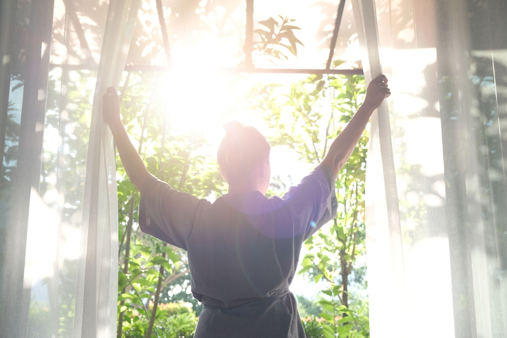 woman opening curtains to let in morning sunlight